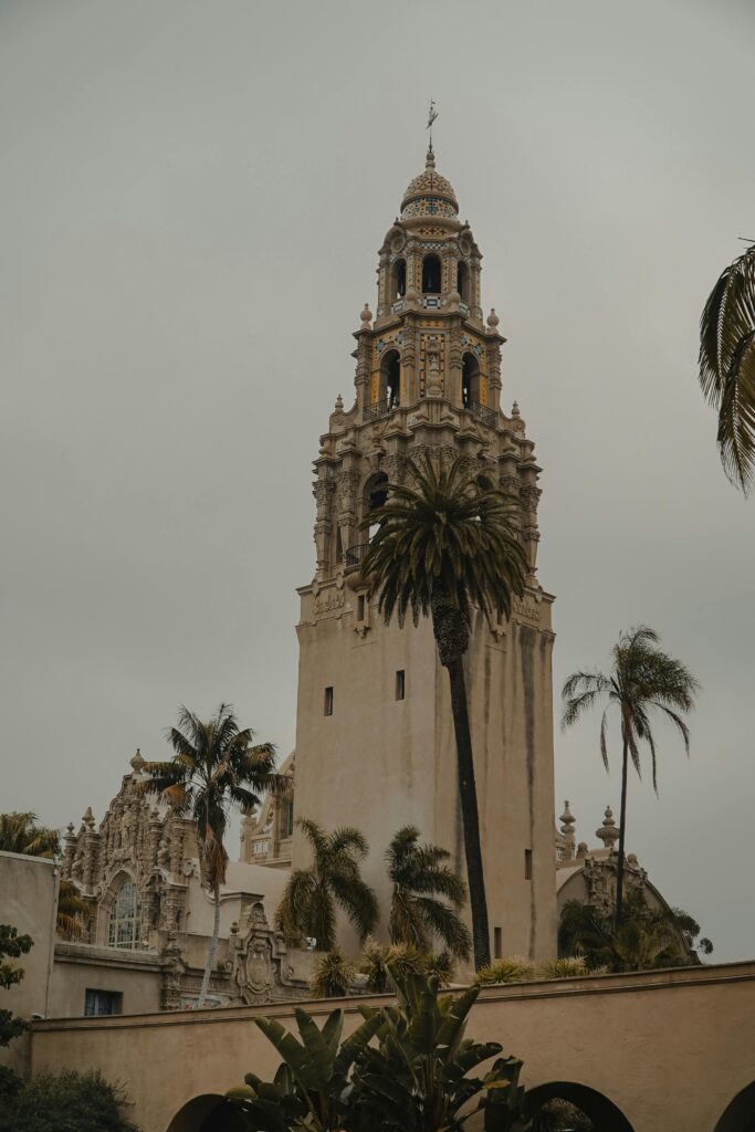 Iconic California Tower in Balboa Park with palm trees on a cloudy day.